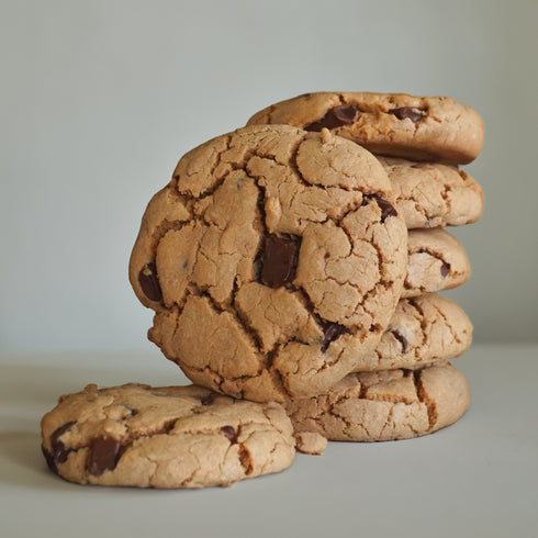 A stack of UniCookies chocolate chunk, The Regular Cookie, with a single cookie standing in front of a stack of cookies.